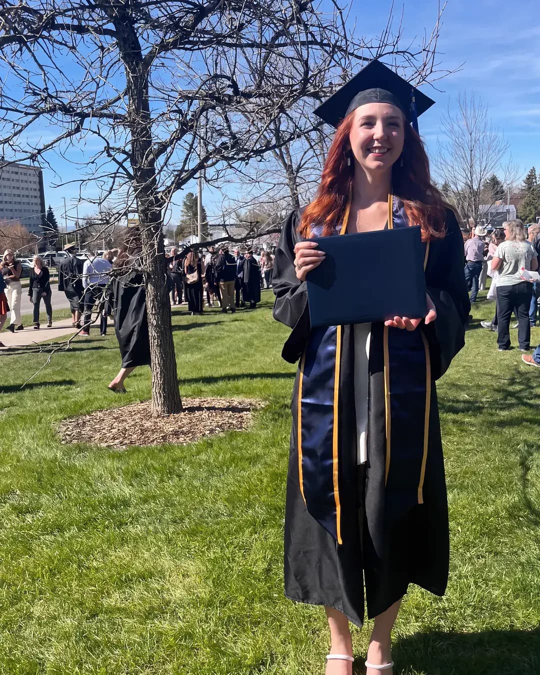 International student in cap and gown holding her diploma on graduation day